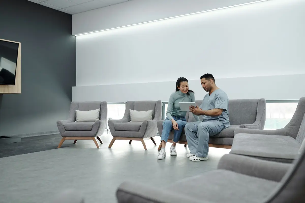 A team member in scrubs talking a patient through information on a tablet in a calm, bright practice lounge