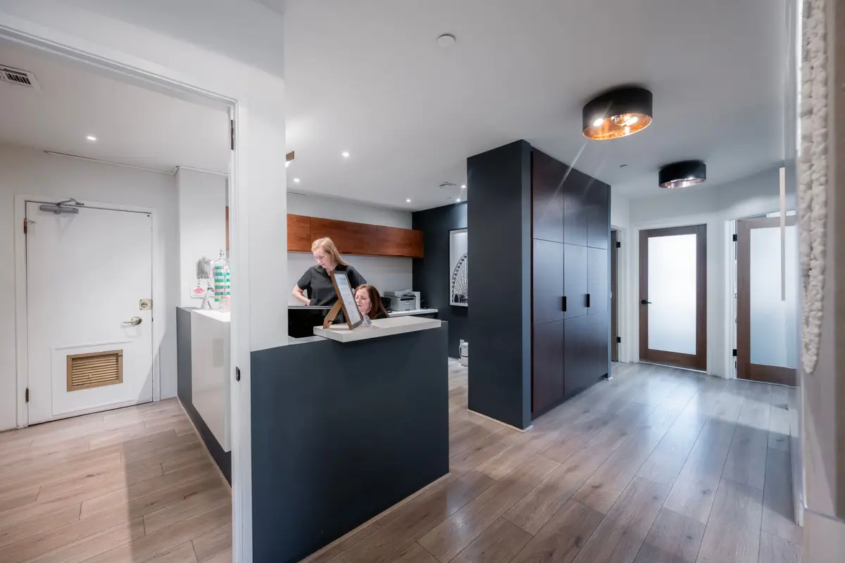 A calm, modern practice reception desk with two team members at work, seen from the hallway