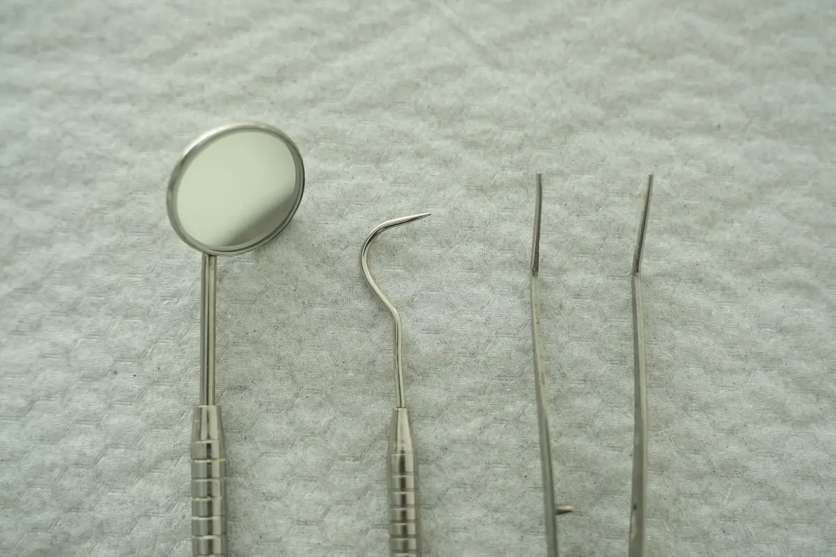 A dental mirror, probe and scaler laid out on a textured surface